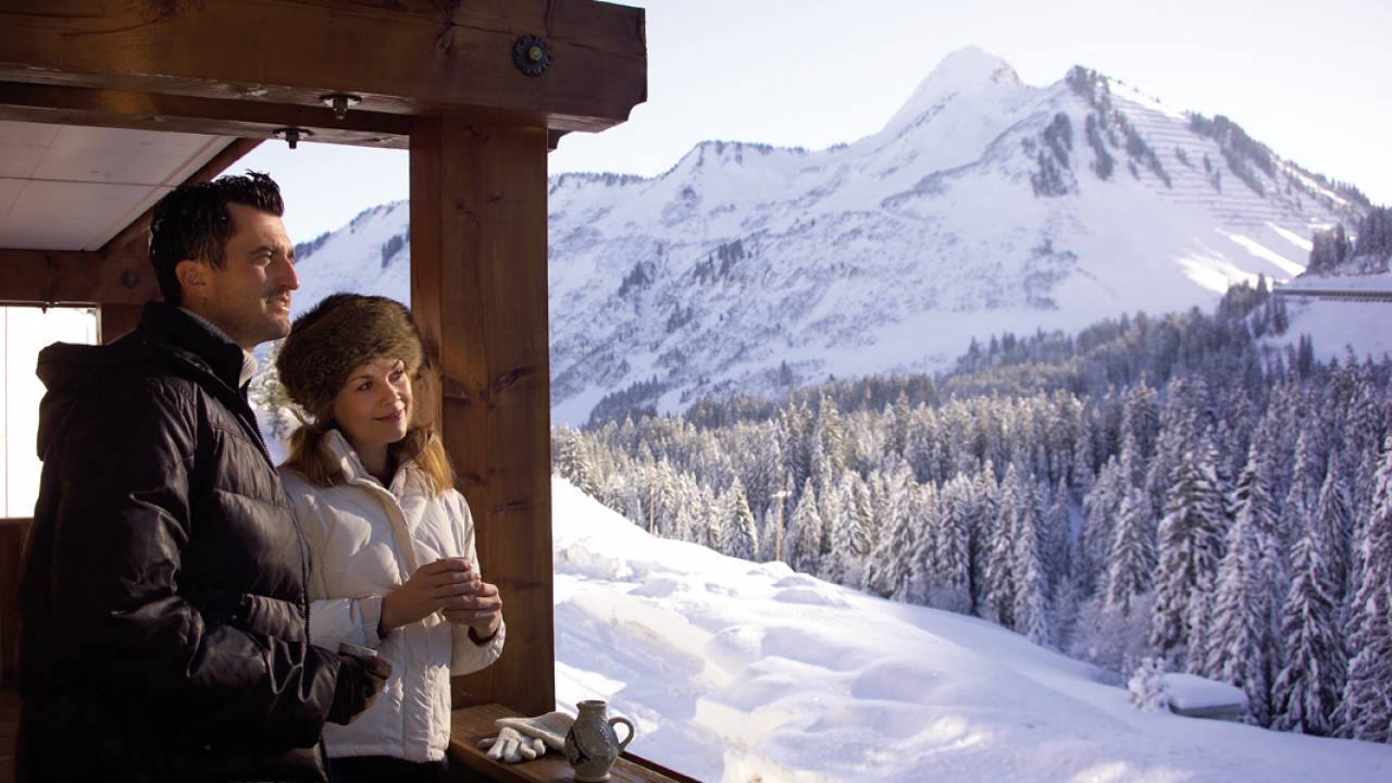 Pärchen genießt verschneite Berglandschaft auf dem Zimmerbalkon